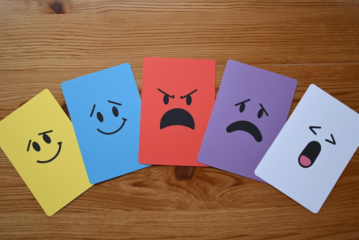 Man sieht 5 Karten in unterschiedlichen Farben, die jeweils für eine andere Emotion stehen. Von links nach rechts: Freude, Mitgefühl, Wut, Angst und Überraschung