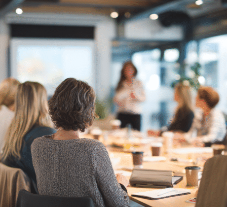 Besprechungsraum mit mehreren Personen, die an einem Tisch sitzen und einer Präsentation zu hören