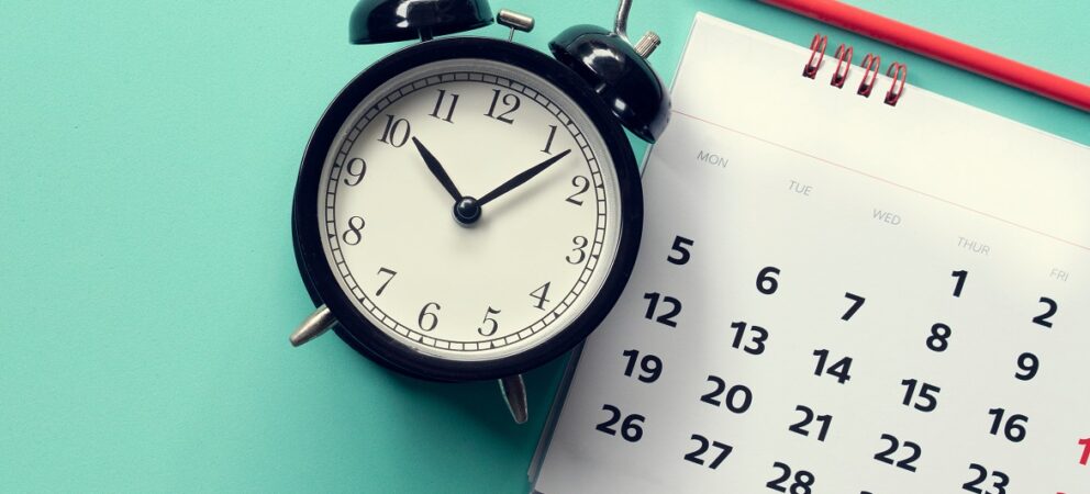 Ein Wecker, ein Kalender und ein Bleistift auf hellblauem Hintergrund.