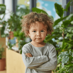 Junge mit Locken hat die Arme vor der Brust verschränkt.