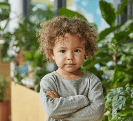 Junge mit Locken hat die Arme vor der Brust verschränkt.