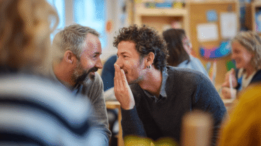 vater flüstert anderem vater etwas ins ohr, symbol: murmelgruppe bei elternabend