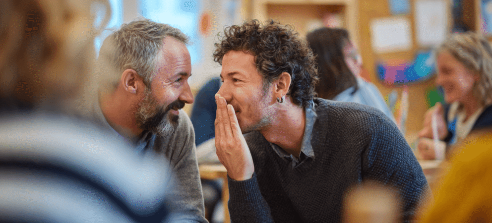 vater flüstert anderem vater etwas ins ohr, symbol: murmelgruppe bei elternabend