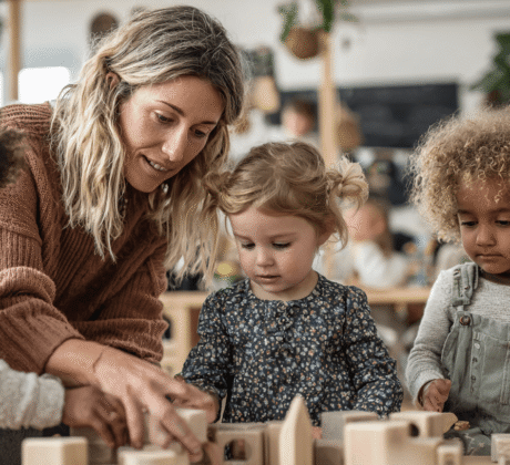 Spielbegleitung von Erziherin mit drei U3-Kindern mit Holzbauklötzen