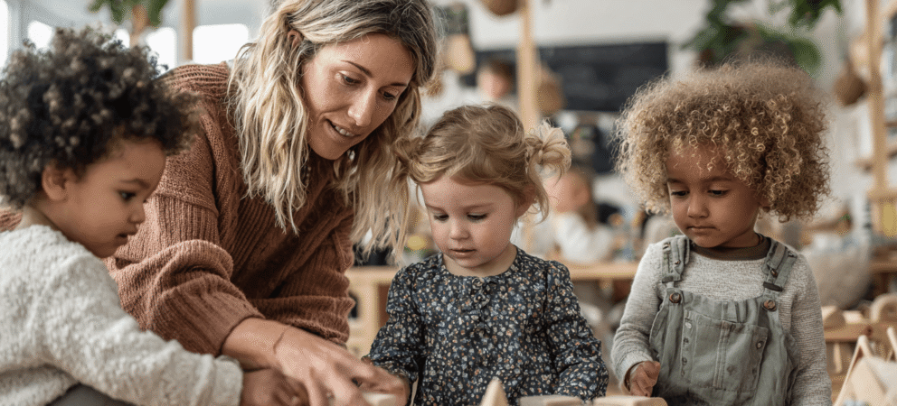 Spielbegleitung von Erziherin mit drei U3-Kindern mit Holzbauklötzen