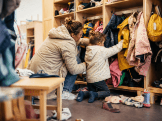 Mutter und Tochter suchen Jacke in Chaos des Kita-Flurs.