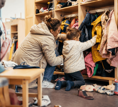 Mutter und Tochter suchen Jacke in Chaos des Kita-Flurs.