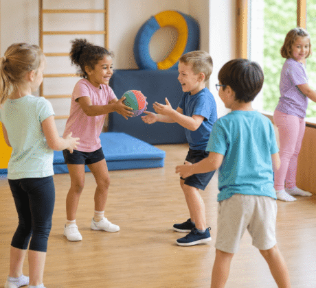 Kinder in Turnhalle werfen sich bunten Ball zu