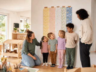 Expertiment in der Kita zum Erkennen von Größenunterschieden, in dem 4 Kinder an die Wand lehnen mit Tapete im Hintergrund