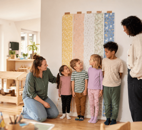 Expertiment in der Kita zum Erkennen von Größenunterschieden, in dem 4 Kinder an die Wand lehnen mit Tapete im Hintergrund