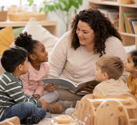 Erzieherin sitzt mit Kindern in Kuschelecke und liest Bücher