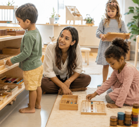 Erzieherin in Montessori-Kindergarten begleitet Kinder im selbstständigen Spiel mit Holz-Materialien.