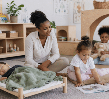 Erzieherin it drei Kindern in Gruppenraum in der Mittagszeit. Eins schläft, ein anderes liest und ein weiteres ist in der Kuschelecke